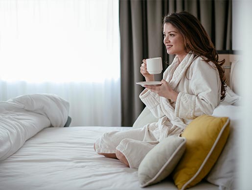 Ospite in accappatoio sul letto che gusta una tazza di caffè in una luminosa camera da letto